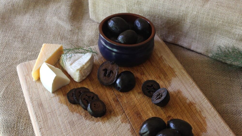Pickled walnuts on a wooden chopping board with cheeses